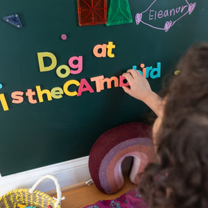 Child playing with large rainbow magnetic letters on green magnetic wall decal