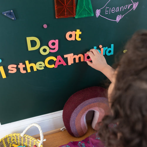 Child playing with large rainbow magnetic letters on green magnetic wall decal