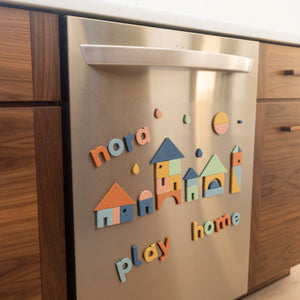 Colorful boho magnetic letters and shapes on a stainless steel dishwasher in a kitchen setting