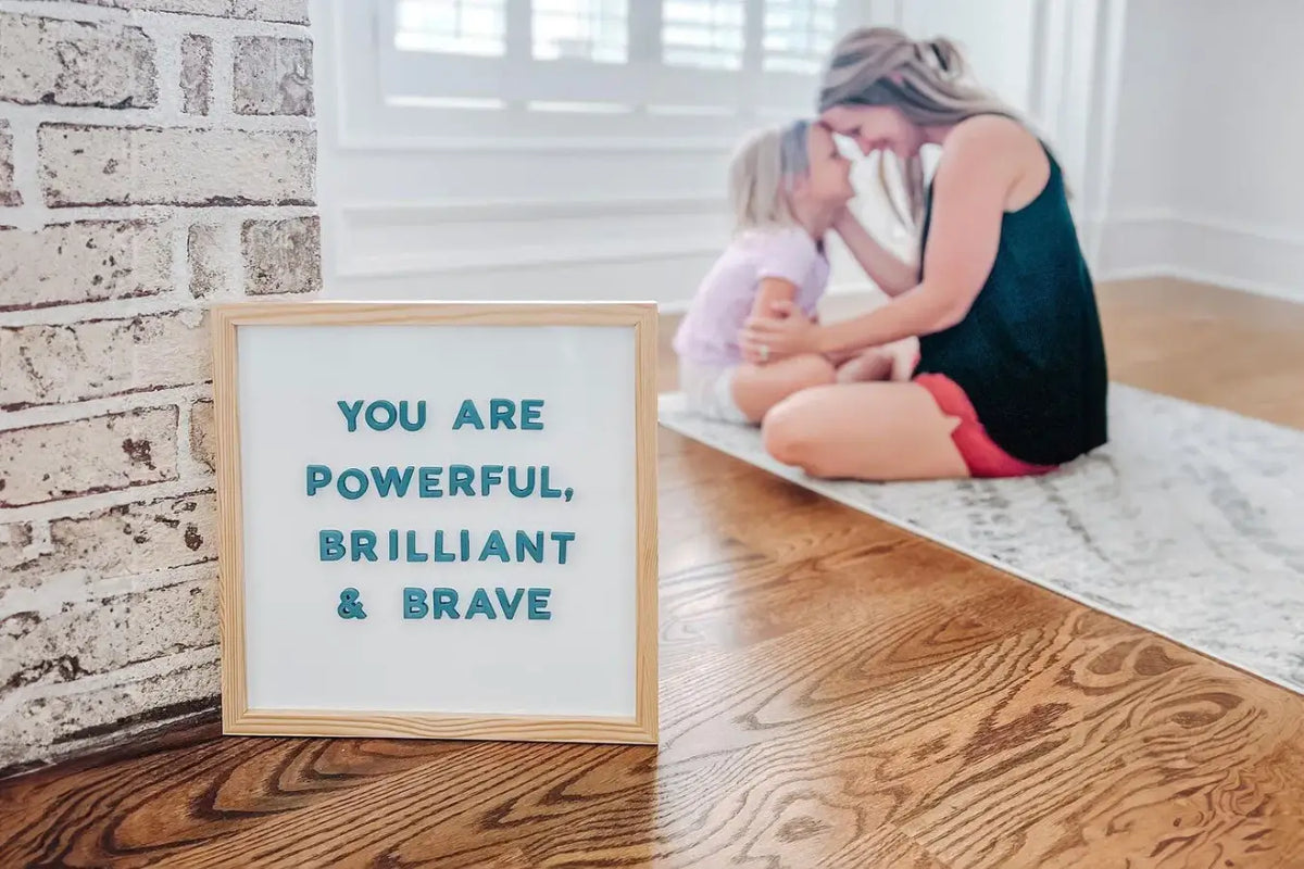 Stylish magnetic letterboard reading “You are powerful, brilliant, and brave” with a parent and child sitting together in the background.