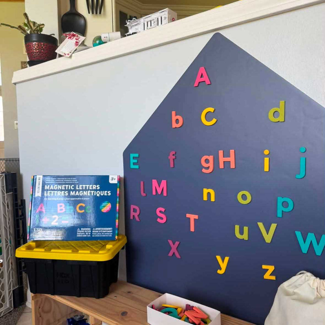 Rainbow magnetic letters on a blue house-shaped wall decal.