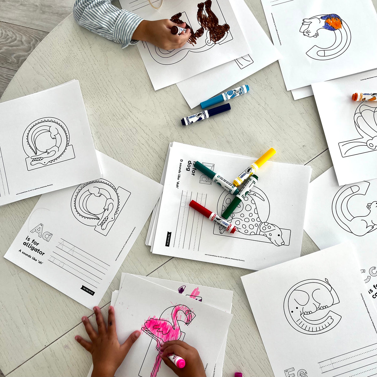 Children coloring printable worksheets with markers on a wooden kitchen tabletop