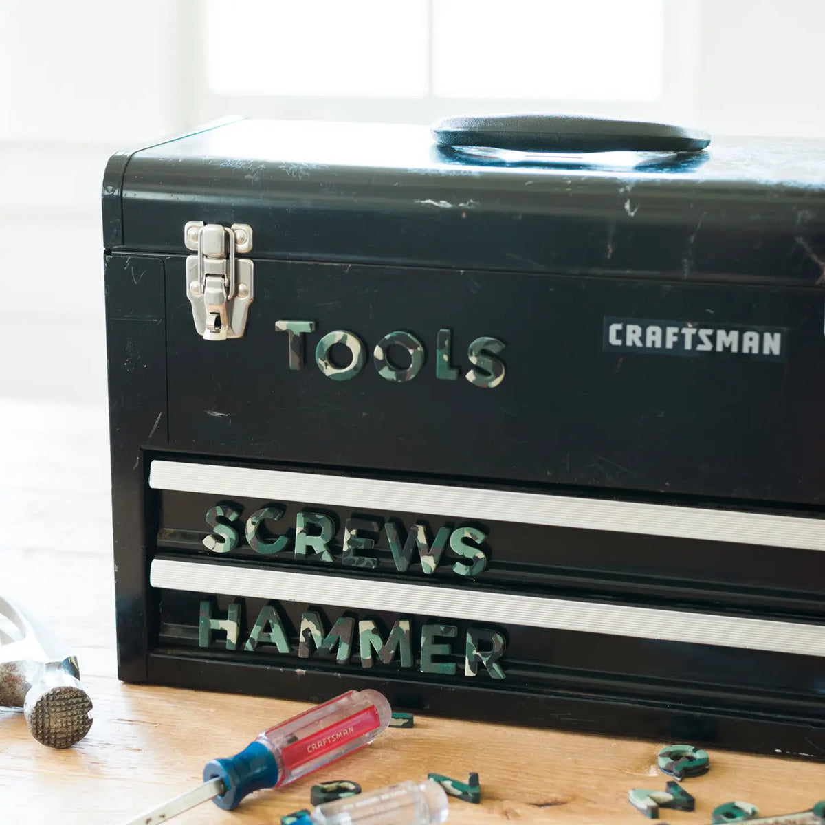 Camo magnetic letters labeling a black metal toolbox with the words TOOLS, SCREWS, and HAMMER