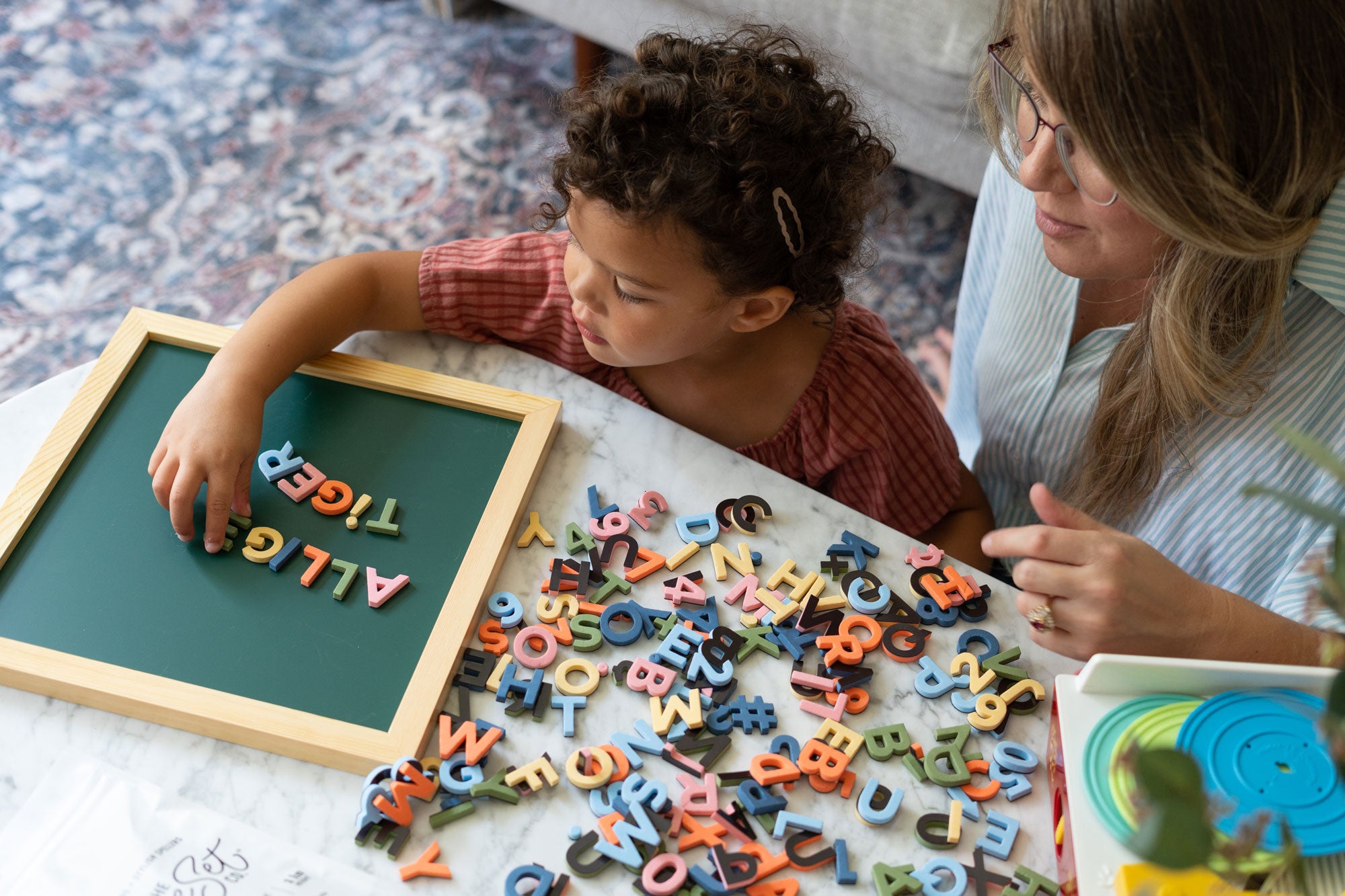 Child and adult playing with colorful magnetic letters on a table.