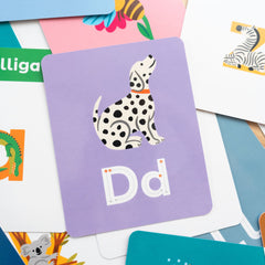 Educational flashcard with a dalmatian dog illustration and traceable letters 'Dd' on a light purple background with other flashcards scattered around it.