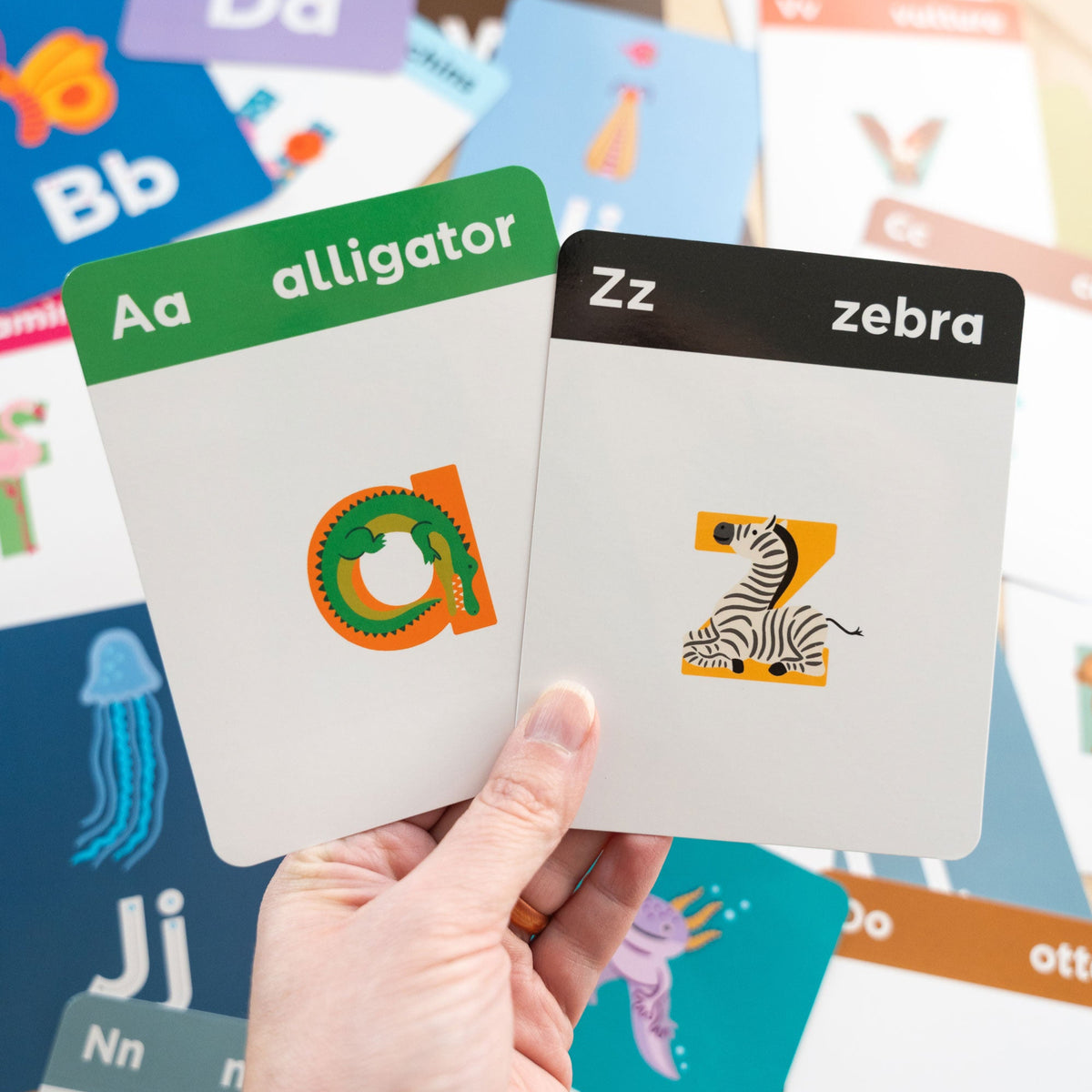 Alphabet flashcards with letters and animals held by a hand, surrounded by more flashcards.