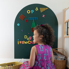 Happy child looking at a colorful set of magnetic letters and magnetic tiles on a green magnetic wall decal