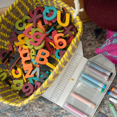 Colorful foam magnetic letters in a basket with stationery items on playroom floor.