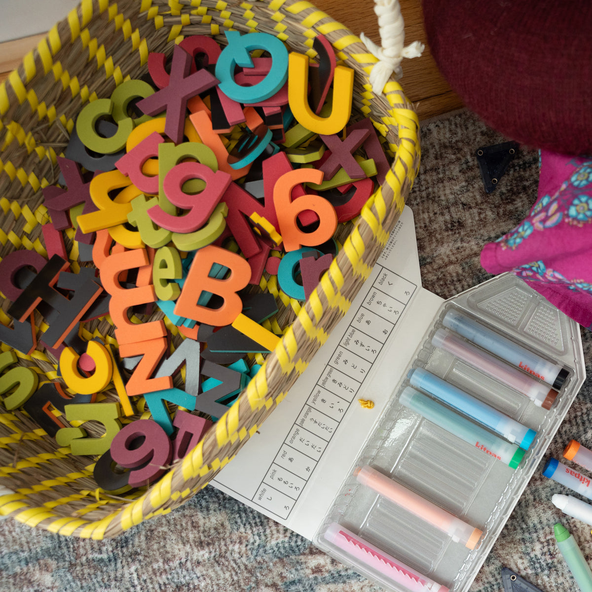 Colorful foam magnetic letters in a basket with stationery items on playroom floor.