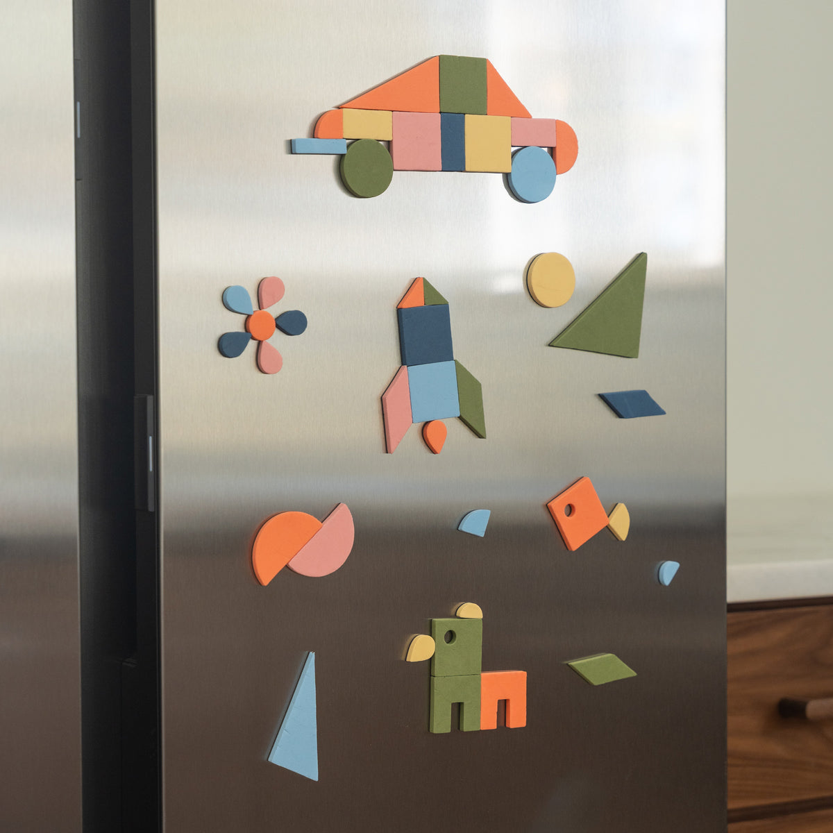 Colorful geometric magnetic shapes making a car, rocjet, fish, and other animal attached to a fridge surface