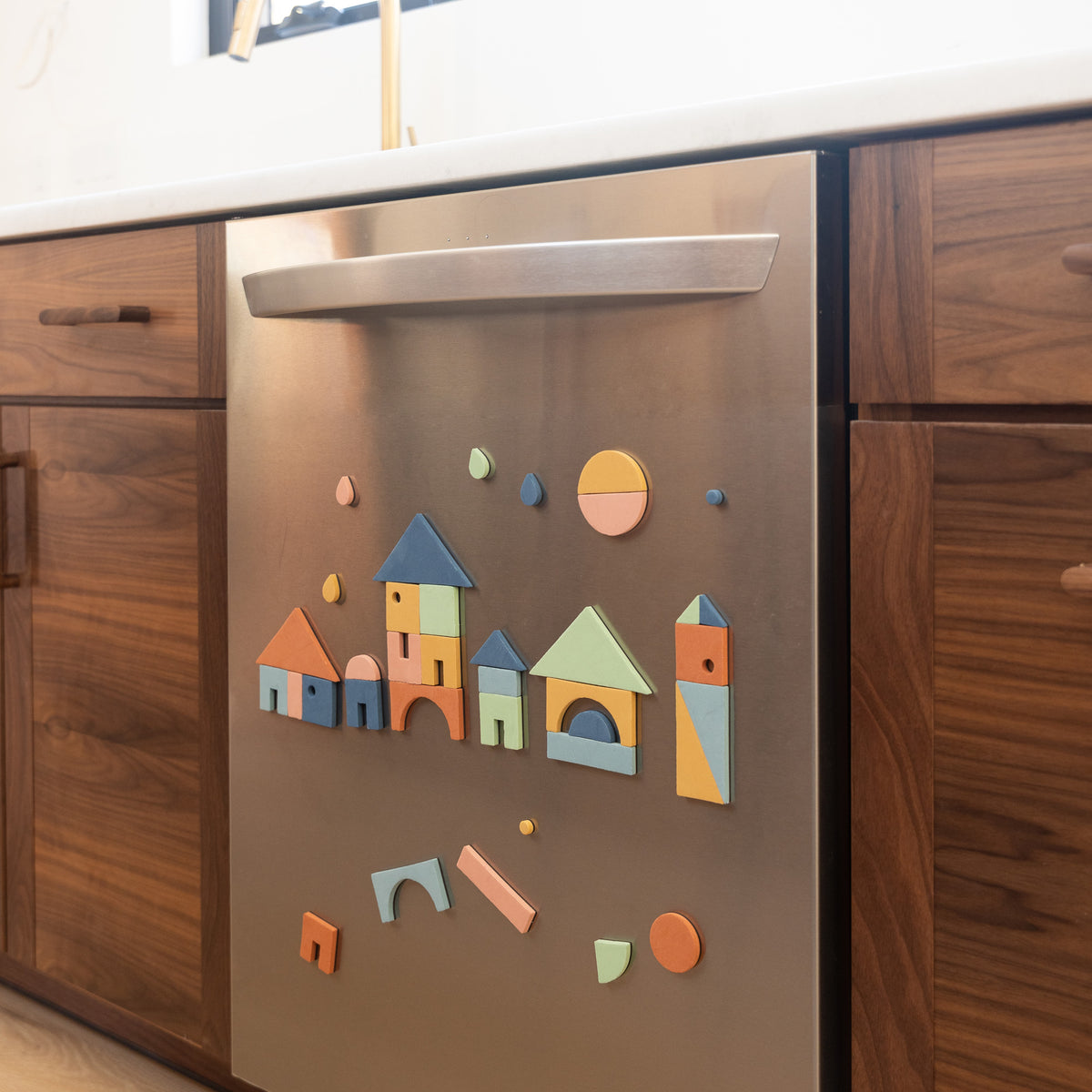 Stainless steel appliance with colorful magnetic shapes next to walnut wood cabinets.