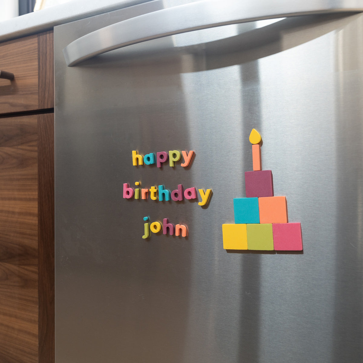 Colorful 'happy birthday john' magnets on a stainless steel dishwasher front