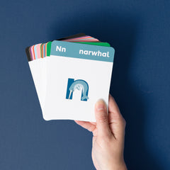 Hand holding a stack of alphabet flashcard swith 'narwhal' and the lowercase letter 'n' and a narwhal illustration against a blue background