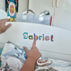 Child spelling his name, Gabriel, using restickable alphabet stickers on the foot of his bed.
