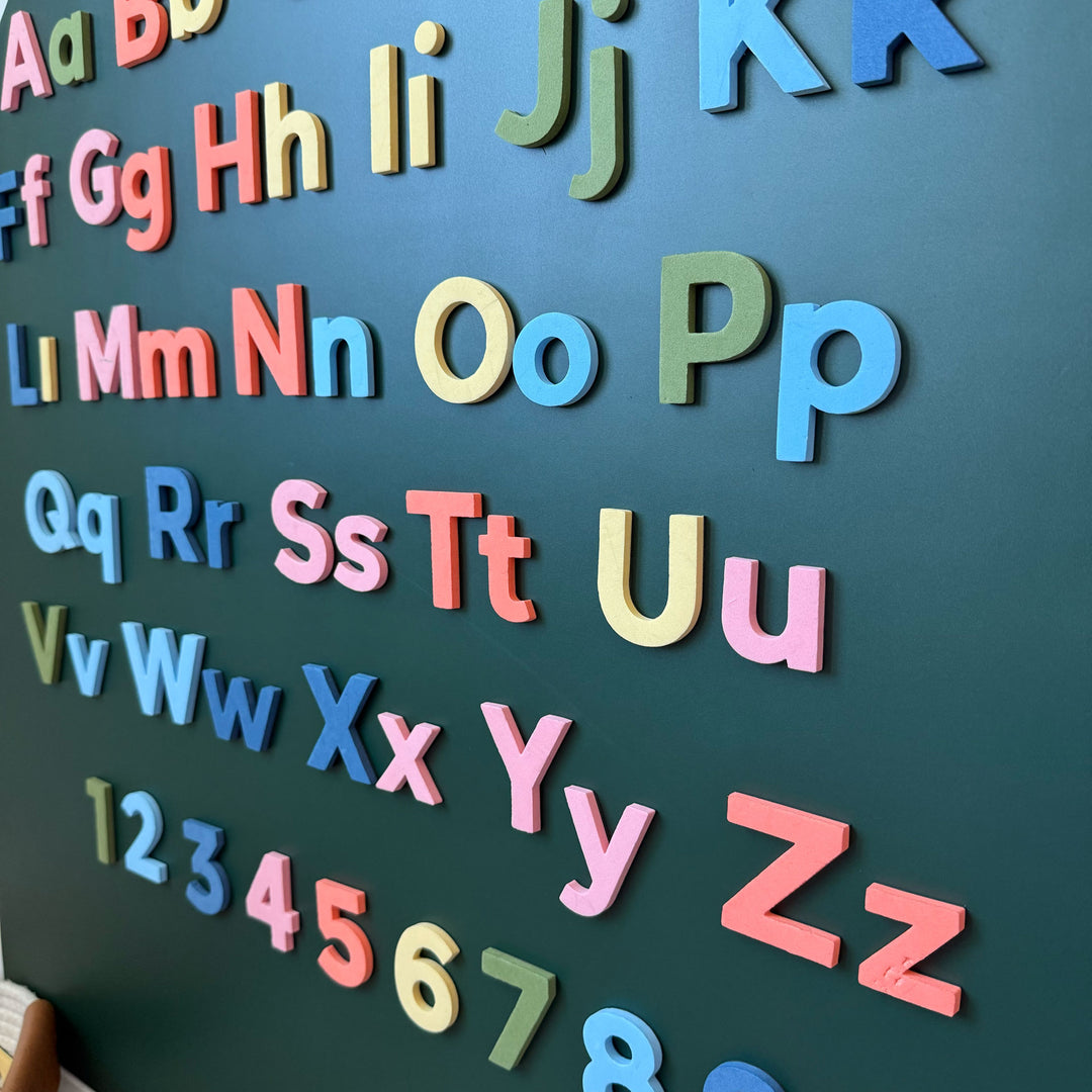 Colorful magnetic alphabet magnets displayed on a dark green wall decal