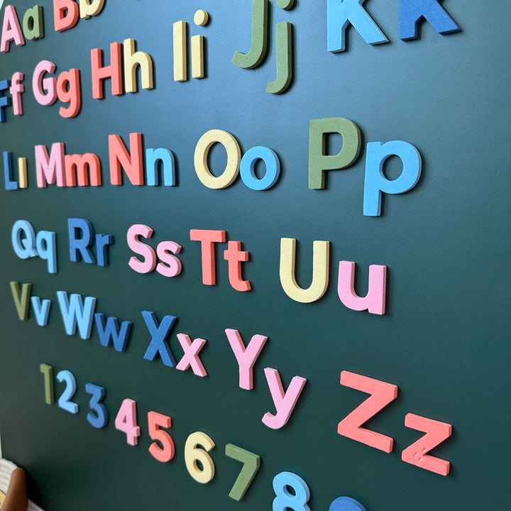 Colorful magnetic alphabet magnets displayed on a dark green wall decal