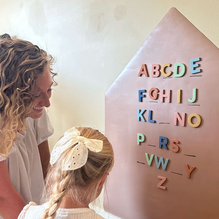 A woman and a young girl are looking at a house-shaped educational wall decal with colorful alphabet magnets.