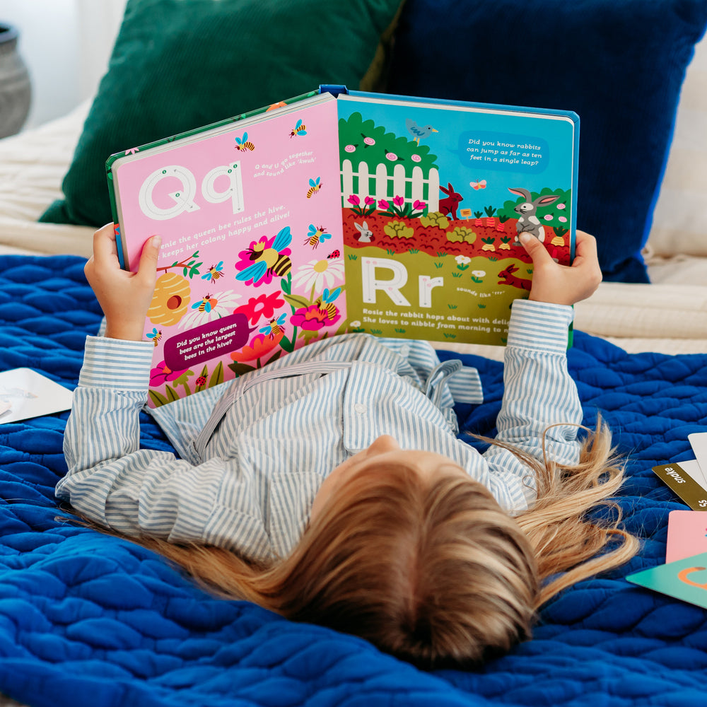 A child lying on a blue blanket, reading a colorful animal alphabet storybook