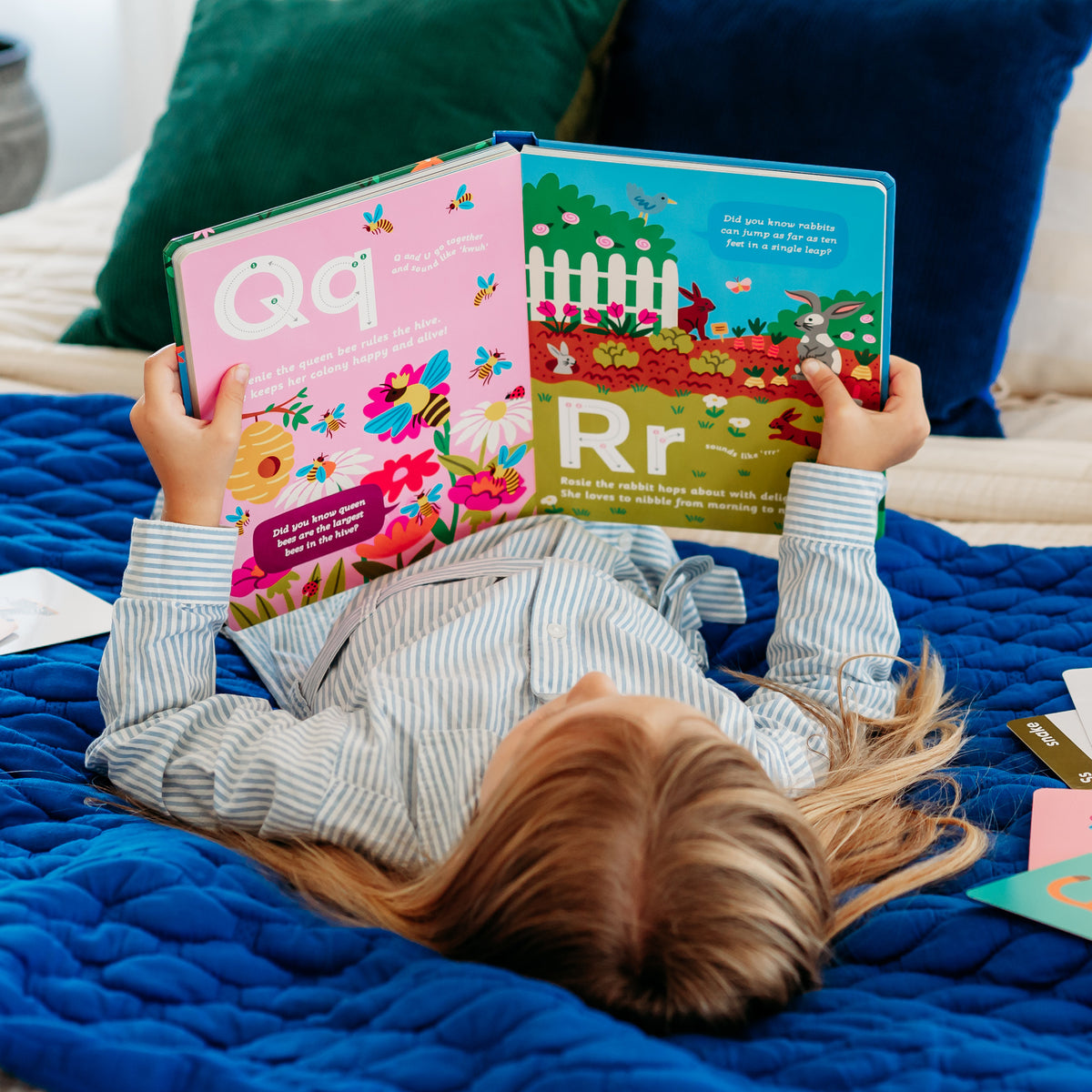 A child lying on a blue blanket, reading a colorful animal alphabet storybook