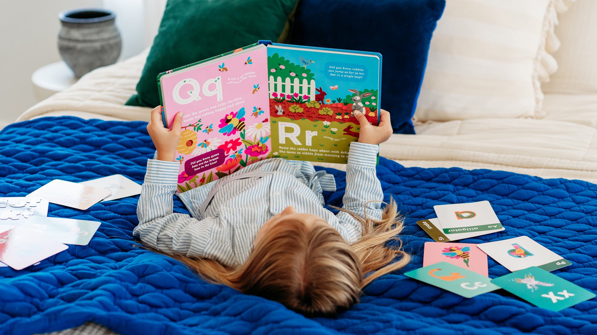 Child reading a an alphabet storybook on a blue blanket with alphabet flashcards cards scattered around