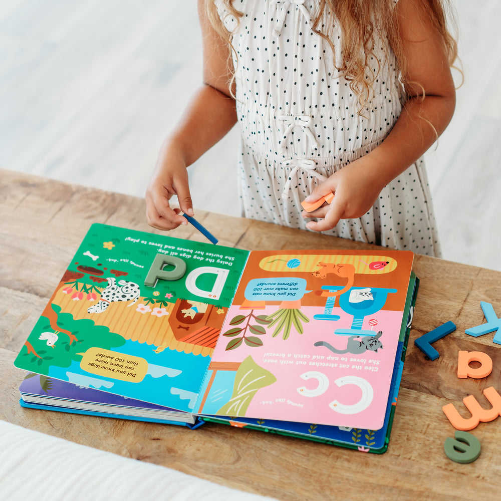 Child matching foam letters with a colorful children's alphabet book on a wooden surface