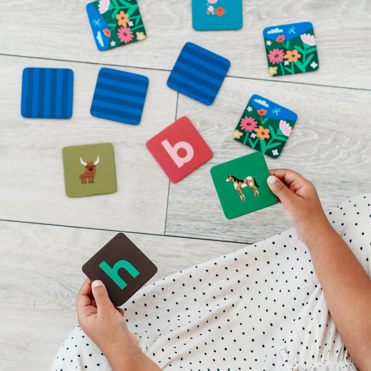 Child playing an educational memory matching game with letters and animals on a light wooden surface