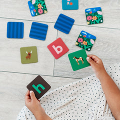 Child playing an educational memory matching game with letters and animals on a light wooden surface