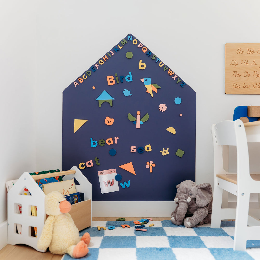 A house-shaped blue magnetic all decal with letters and words and shapes on a white wall in a children's room. 