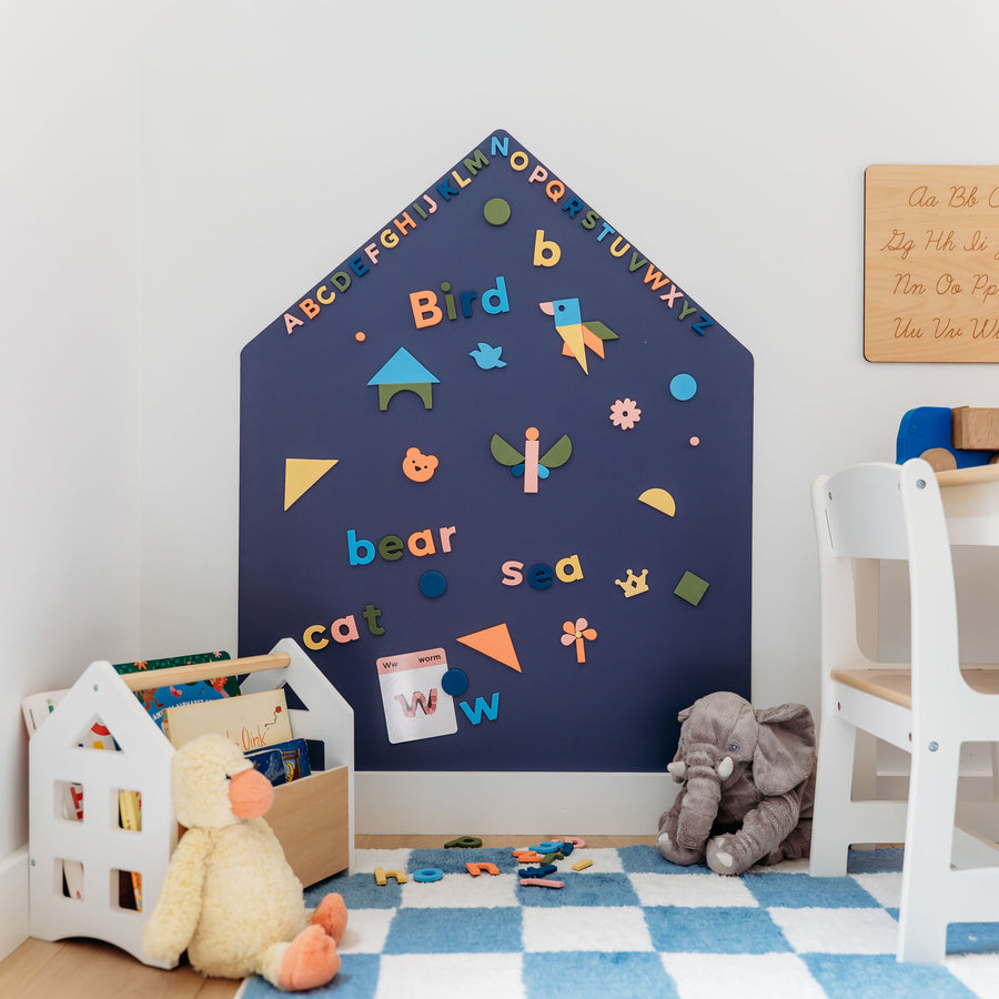 A house-shaped blue magnetic all decal with letters and words and shapes on a white wall in a children's room. 