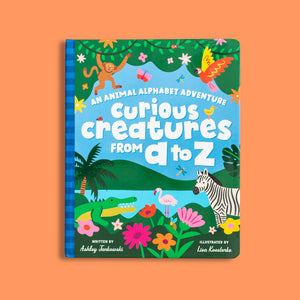 Children's book cover titled 'Curious Creatures from A to Z' with colorful illustrations of animals and plants in a jungle scene with lake and mountains 
