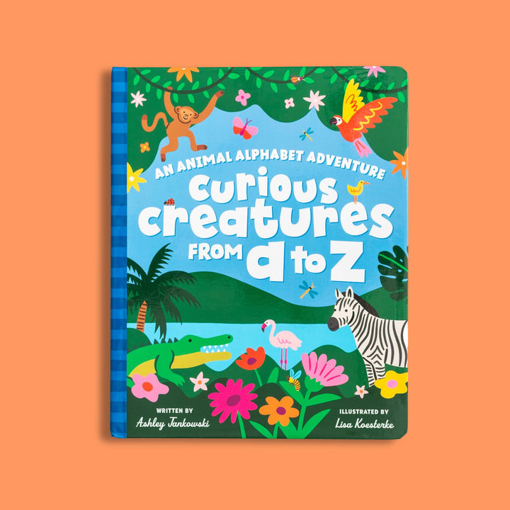 Children's book cover titled 'Curious Creatures from A to Z' with colorful illustrations of animals and plants in a jungle scene with lake and mountains 