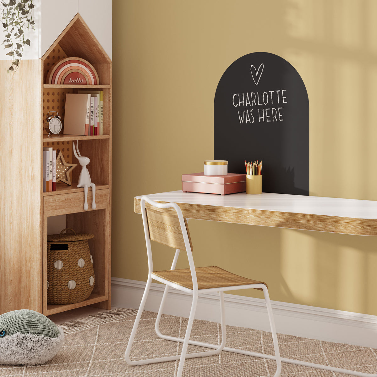 Children's room with wooden desk, chair, and bookshelf against a yellow wall with black magnetic wall decal with chalk writing 'CHARLOTTE WAS HERE'