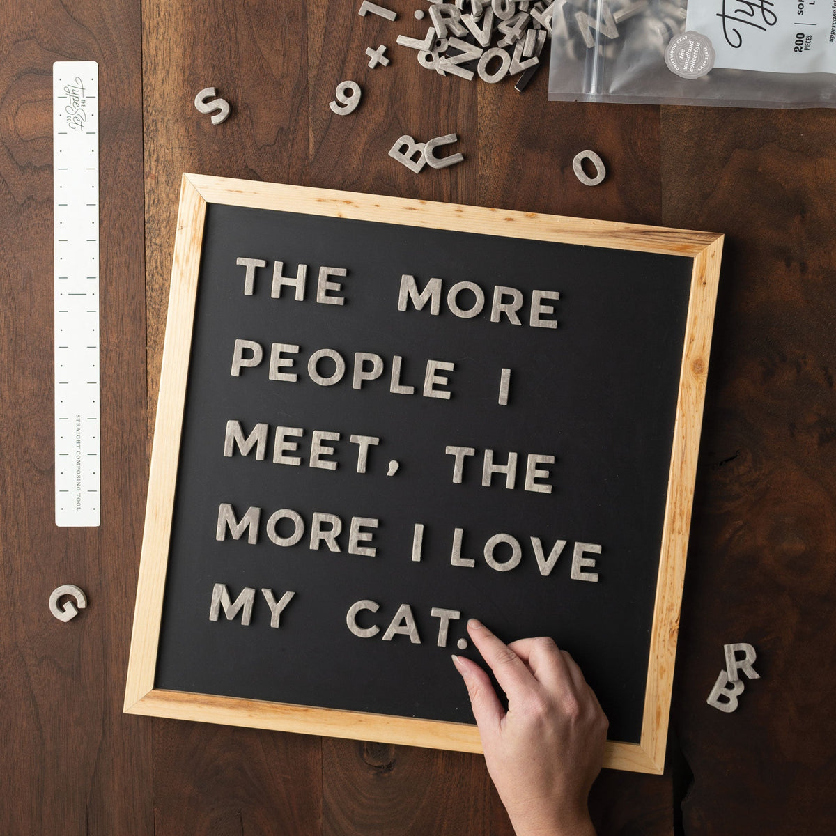 Gray faux wood magnetic letters spelling THE MORE PEOPLE I MEET, THE MORE I LOVE MY CAT on a black magnetic board